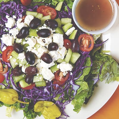 greek salad on plate with side of dressing